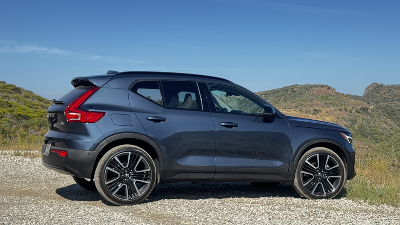 A side view of the blue XC40 parked on gravel in front of a view of shrub-covered mountains and a blue sky