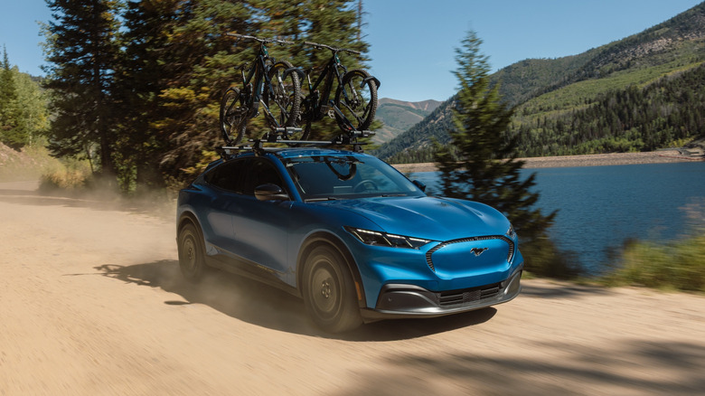 A blue 2027 Ford Mustang Mach-E Trail driving down a dirt road.