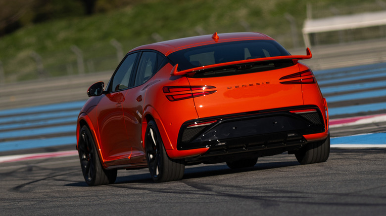 Rear 3/4 view of an orange Genesis GV60 Magma on track