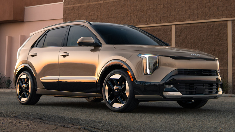 A front three-quarters shot of a brown Kia Niro parked in front of a brick building