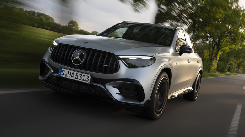 A front three quarters shot of a silver AMG GLC53 driving on a rural road past trees and grass
