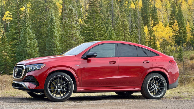 Side view of a red GLE53 coupe parked on dirt in front of green and yellow trees