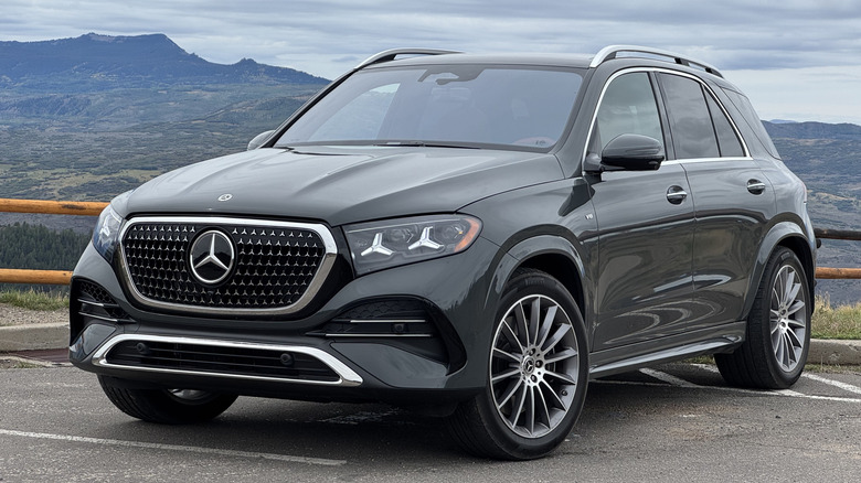 Front three-quarters shot of a gray GLE580 parked on asphalt in front of a view of a cloudy sky and mountain range