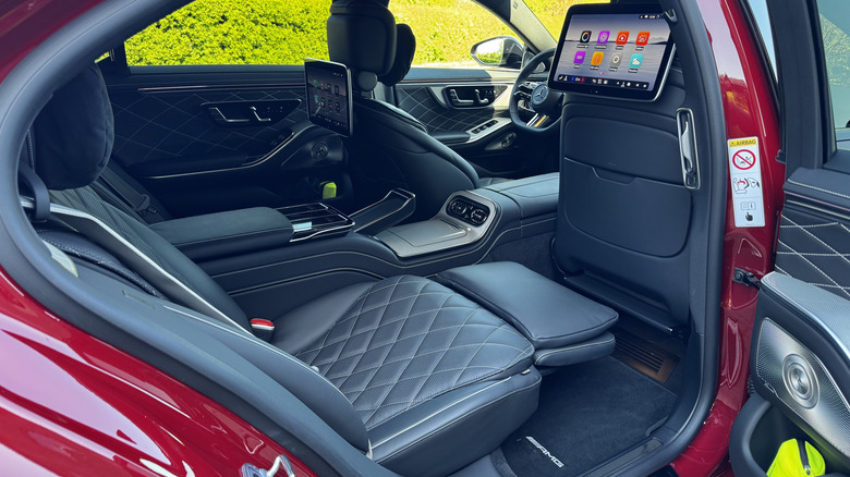 A look in the rear door at the black leather rear seat with its foot rest up and the screen on the back of the passenger seat visible