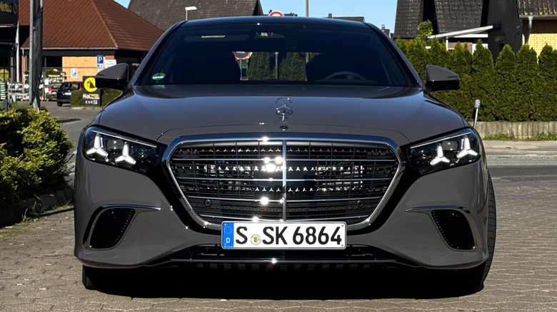 A head-on shot of a gray S500 parked on bricks in front of a street and hedge