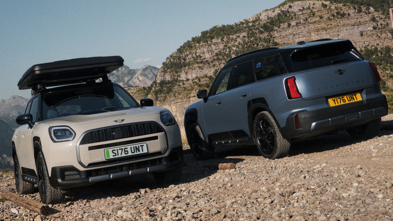 A gray Countryman SE Untamed with a rooftop tent parked facing the camera next to a matte blue Countryman S Untamed parked nose-in on rocks in front of mountains