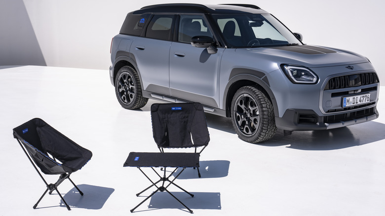 A matte blue Countryman S Untamed Edition parked on a white surface behind the Untamed black folding camping equipment