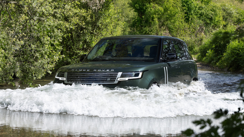A green Range Rover Electric wading through water