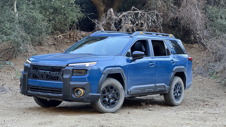 front three-quarters view of a dark blue Outback Wilderness parked on dirt in front of trees