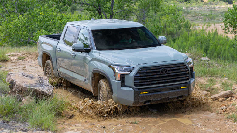 Front three-quarters shot of a gray Tundra with the Trailhunter Package driving through a muddy puddle on an off-road trail