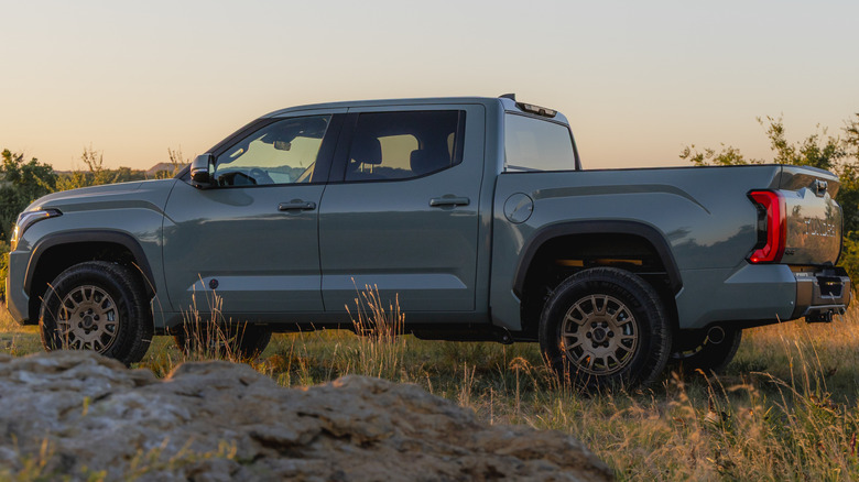 A side view of the gray 2027 Tundra with the Trailhunter Package parked on grass at sunset with a rock in the foreground