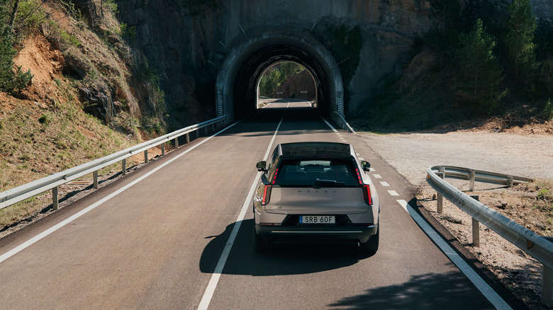 A silver 2027 Volvo EX60 approaching a mountain tunnel