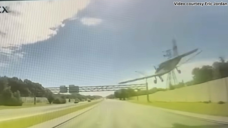 A video of a dashcam video with a plane coming down towards a highway and sign.