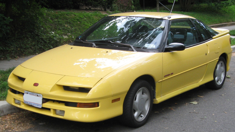 A yellow Geo Storm parked on a suburban street.