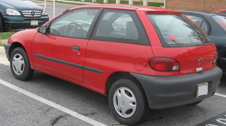 A bright red Chevrolet Metro two-door hatchback, situated in a parking lot.