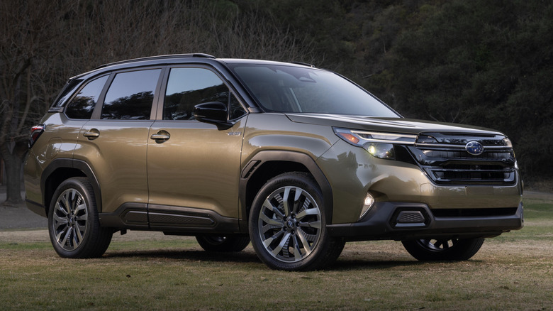 A gold 2025 Subaru Forester Hybrid parked in front of tree-covered hills