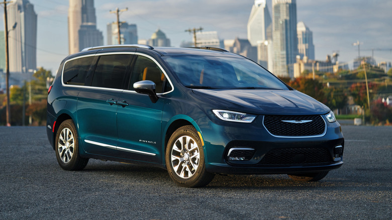 A blue Chrysler Pacifica Hybrid parks against a city skyline.