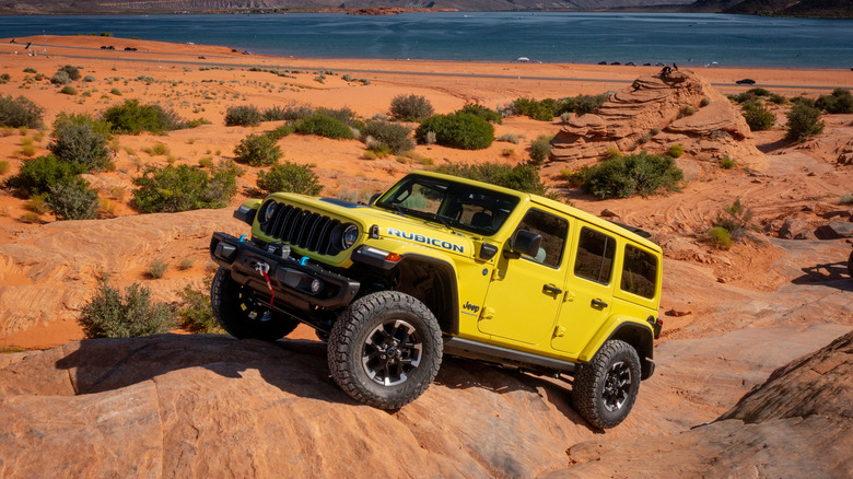 A yellow Jeep Wrangler 4xe climbs steep rocks with a lake in the background