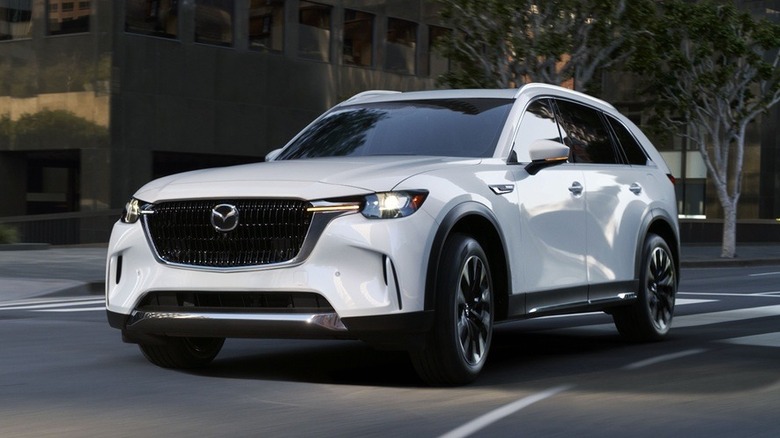 A white Mazda CX-90 PHEV navigates a turn in the city.