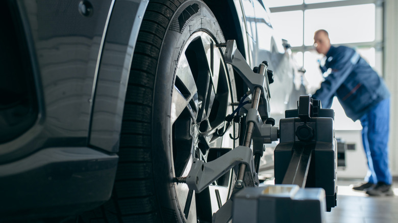 A technician adjusting the wheel alignment of a vehicle using a computer and wheel sensors
