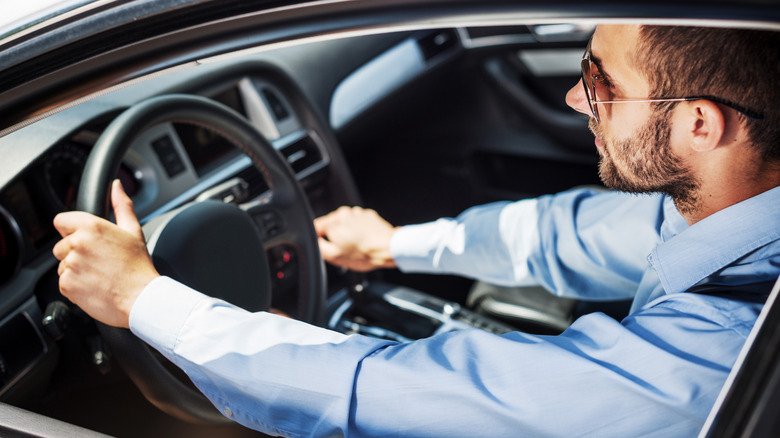 A young man driving a car with one hand on the steering wheel