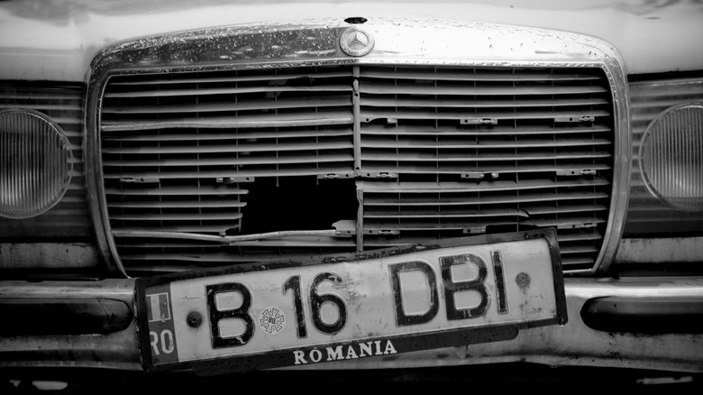 A zoomed-in photo of an old Mercedes-Benz with a hole in its grille and a Romania license plate.