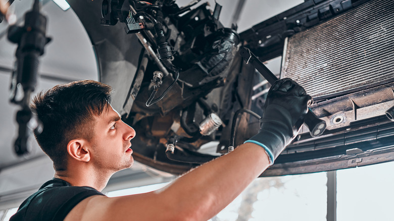 A mechanic is curiously examining car radiator inside of a garage.