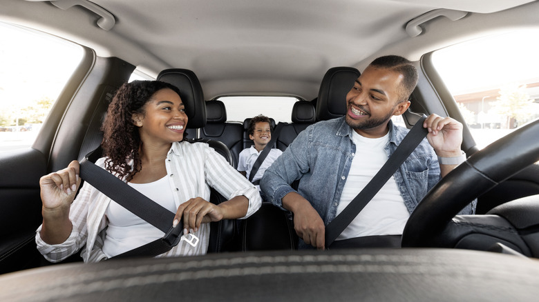 A family of three all being buckled up while in a stationary car.