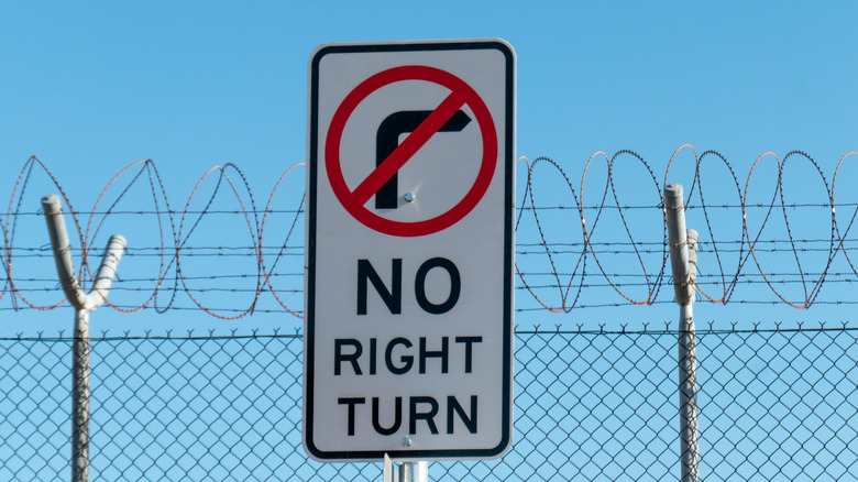 A no right turn traffic sign with barbed wire and blue skies in the background.