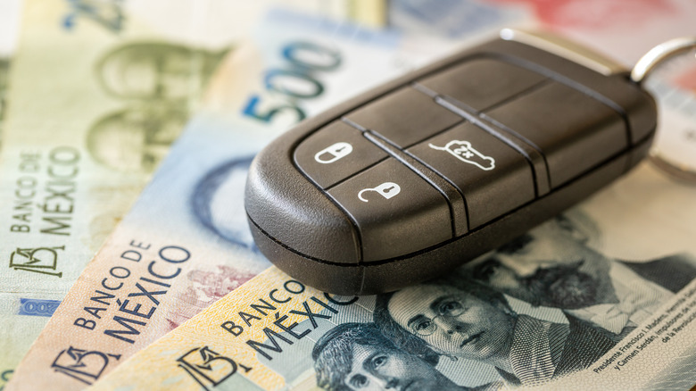 A car key resting on Mexican pesos.