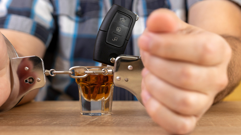 A person in handcuffs with a car key resting in a tequila shot.