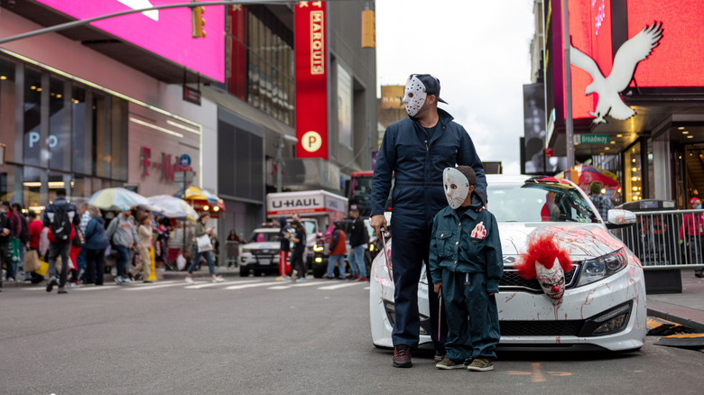 A child and an adult wearing Halloween costumes standing in front of a car.