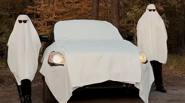 Two people dressed in ghost costumes posting near a car looking like a ghost.