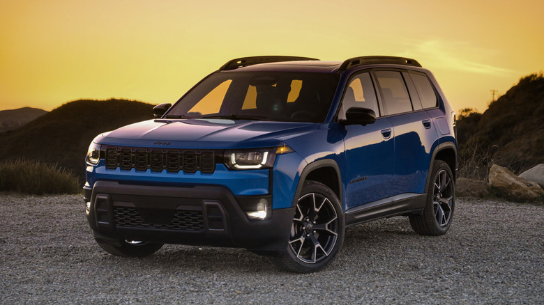 A blue 2026 Jeep Cherokee parked on a gravel trail at golden hour with hills in the background.