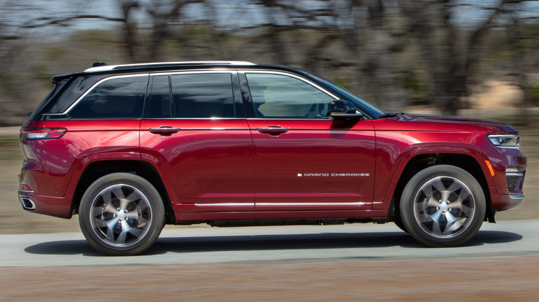 A red 2022 Jeep Grand Cherokee driving down a road past bare trees.