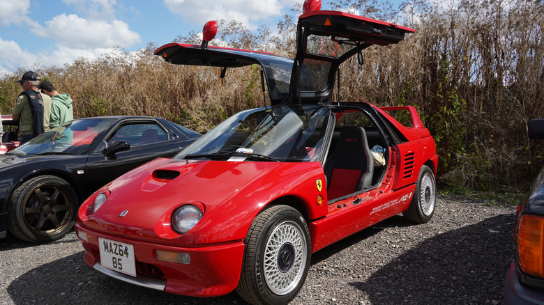 A red Autozam AZ-1 kei car parked with its gull-wing doors up.