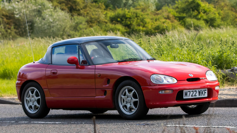 A red Suzuki Cappuccino kei car being driven on an English country road.