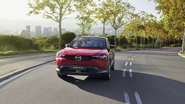 A red Mazda MX-30 drives on a bend.