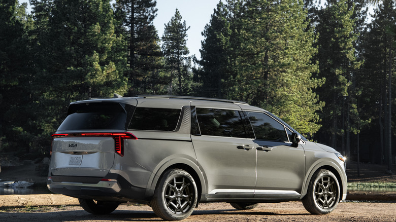 The Kia Carnival parked on a dirt road in front of a forest