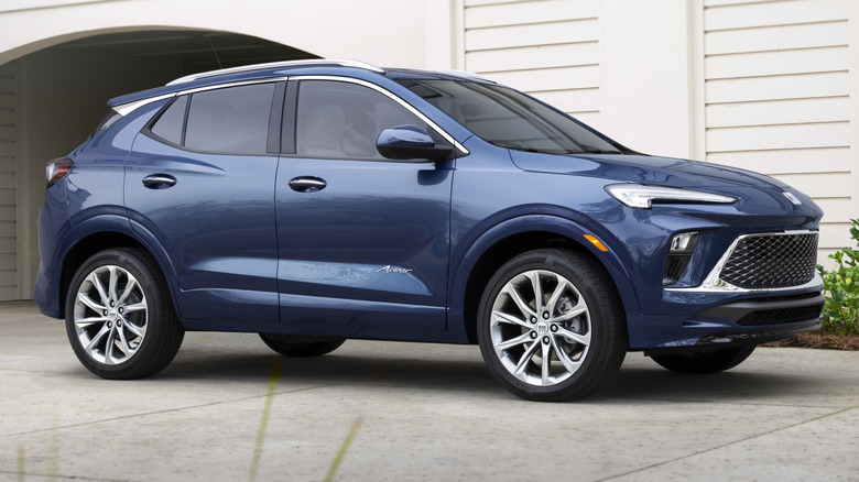 The right-side profile of a blue Buick Encore GX Avenir in front of a building
