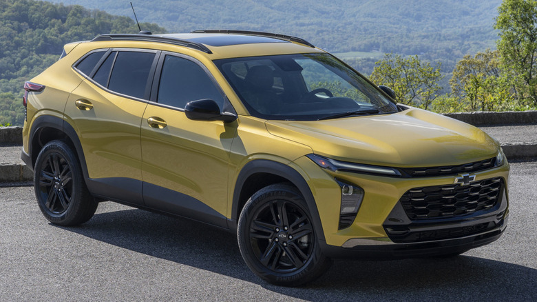 The front 3/4 view of a Nitro Yellow Metallic Chevy Trax parked on a road with mountains in the background