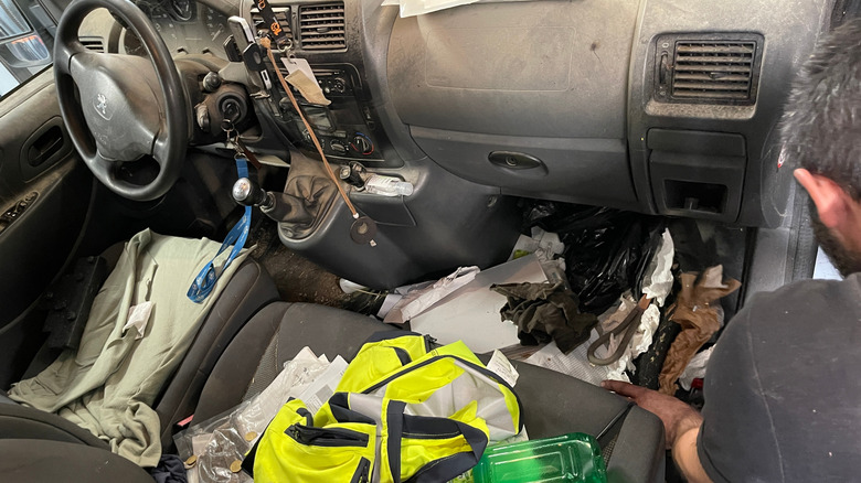 The interior of a messy car with trash covering the floor