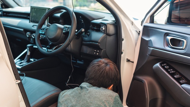 A person working under the car's dash with the car door open.