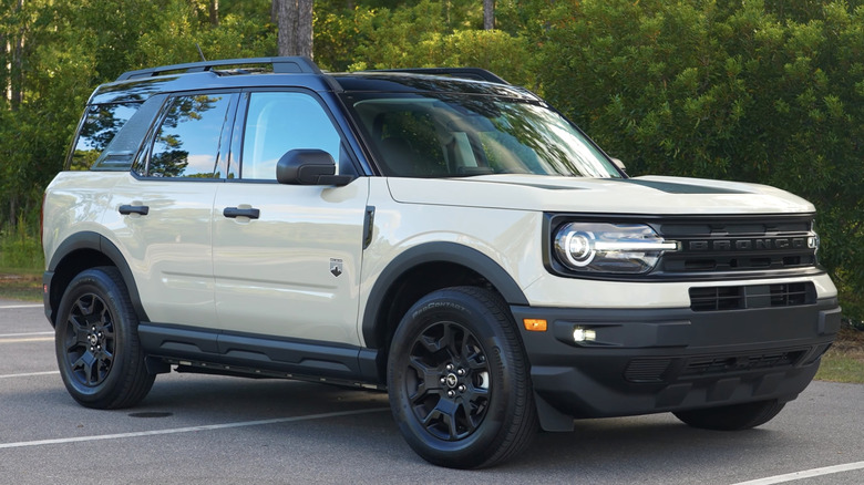 A tan Ford Bronco Sport sits parked in an empty lot with trees in the background