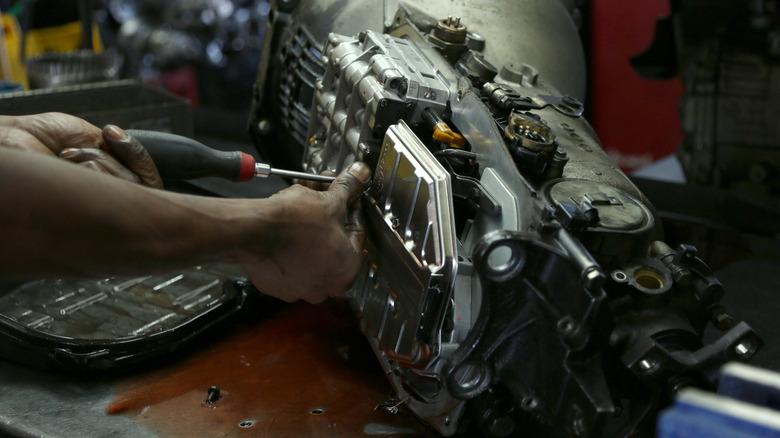 A mechanic's hands working on a transmission removed from a car