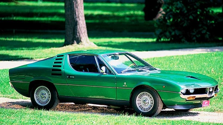 An emerald green Alfa Romeo Montreal sports car parked on a gravel driveway on a lawn.
