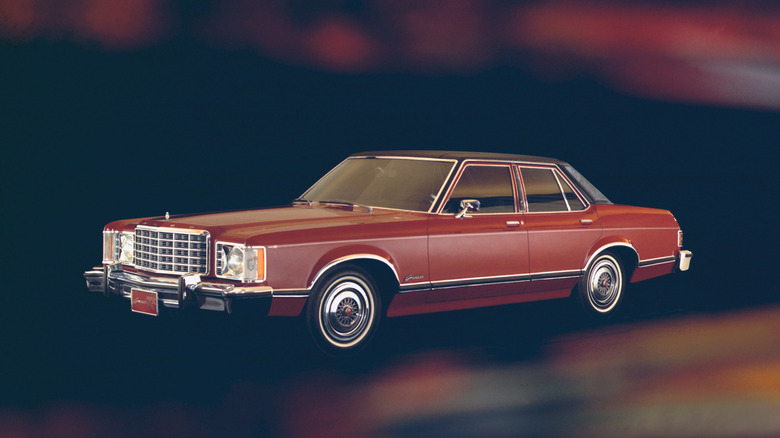 A red 1975 Ford Granada four-door sedan with a black vinyl roof, wire wheel covers, and chrome grille against a dark, moody background.