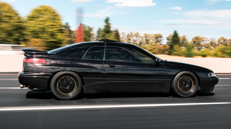 A side shot of a black Subaru SVX driving down a road