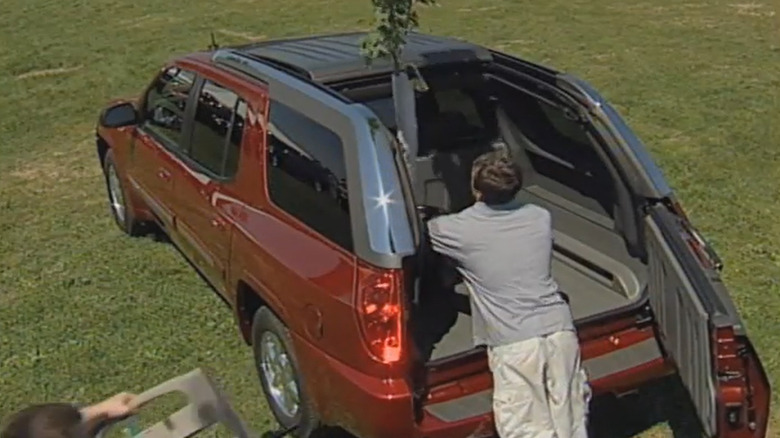 A man loads a potted tree into the back of a red GMC Envoy XUV