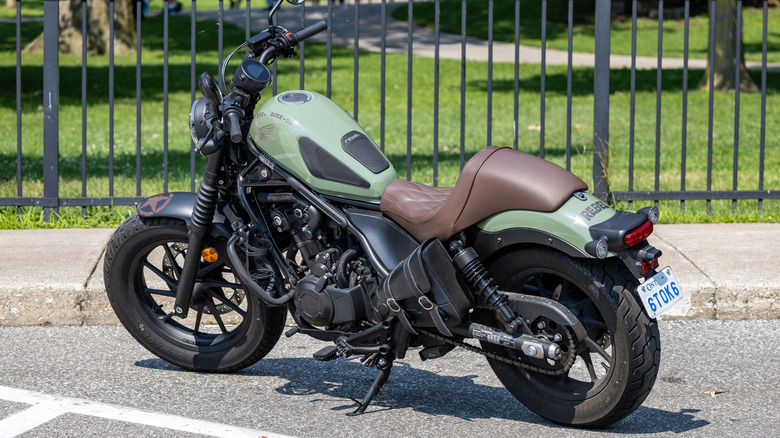 A green and black Honda Rebel is parked on the street in front of a black metal fence
